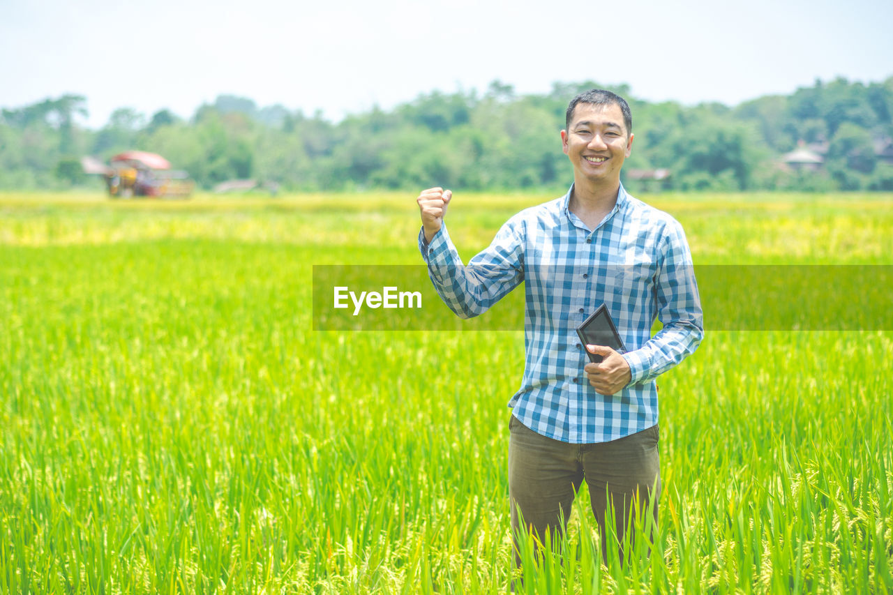 Portrait of smiling man on field holding digital tablet
