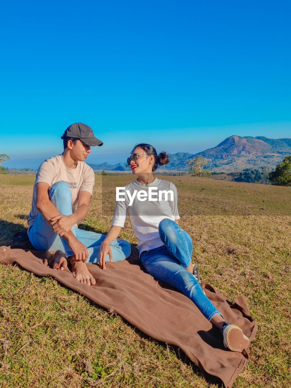 Full length of couple sitting on land against blue sky