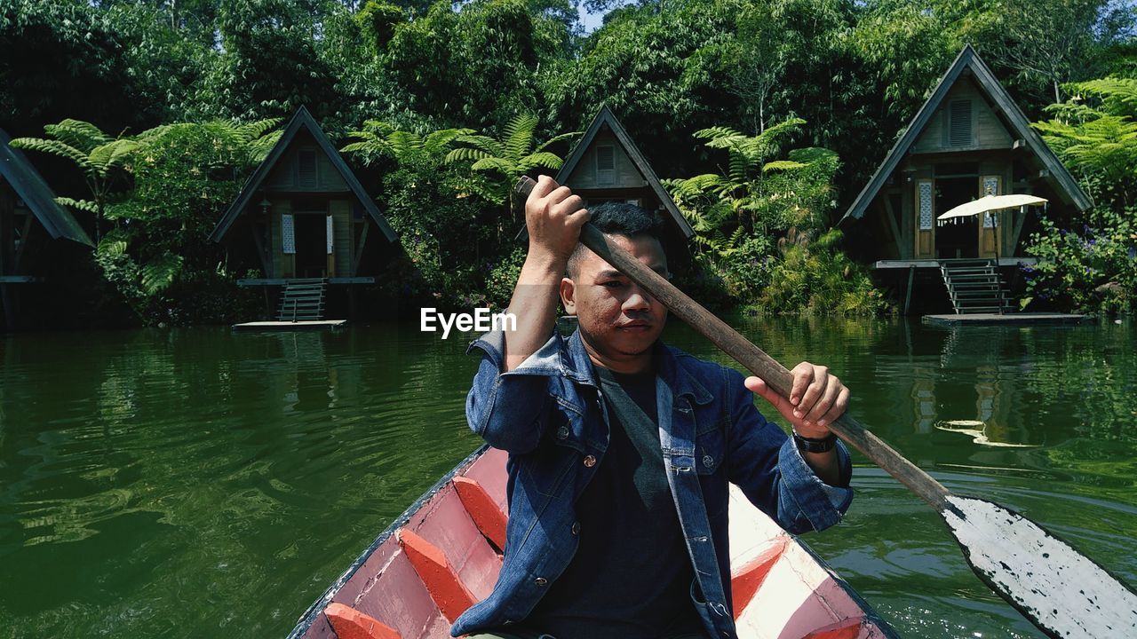 Portrait of young man rowing boat on lake against trees