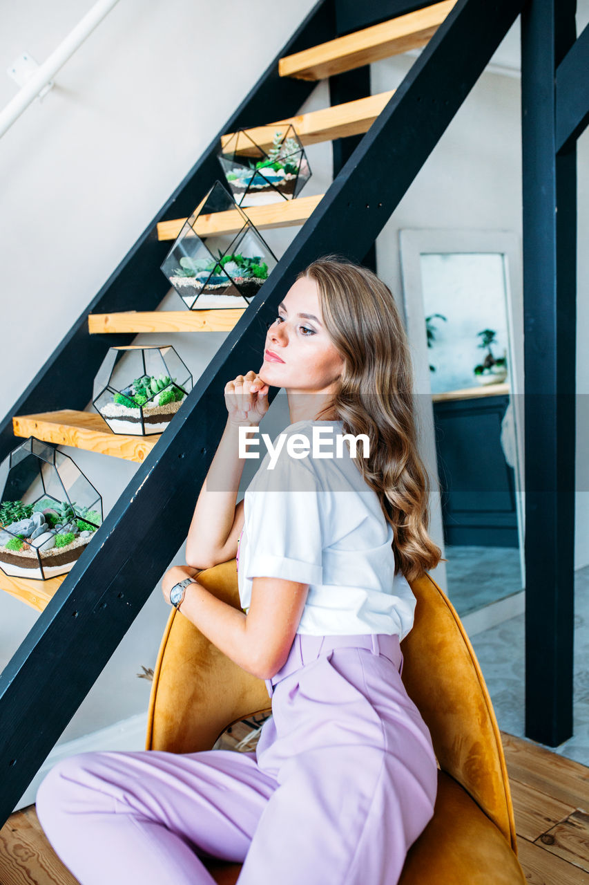 YOUNG WOMAN LOOKING AT WHILE SITTING ON SOFA AT HOME