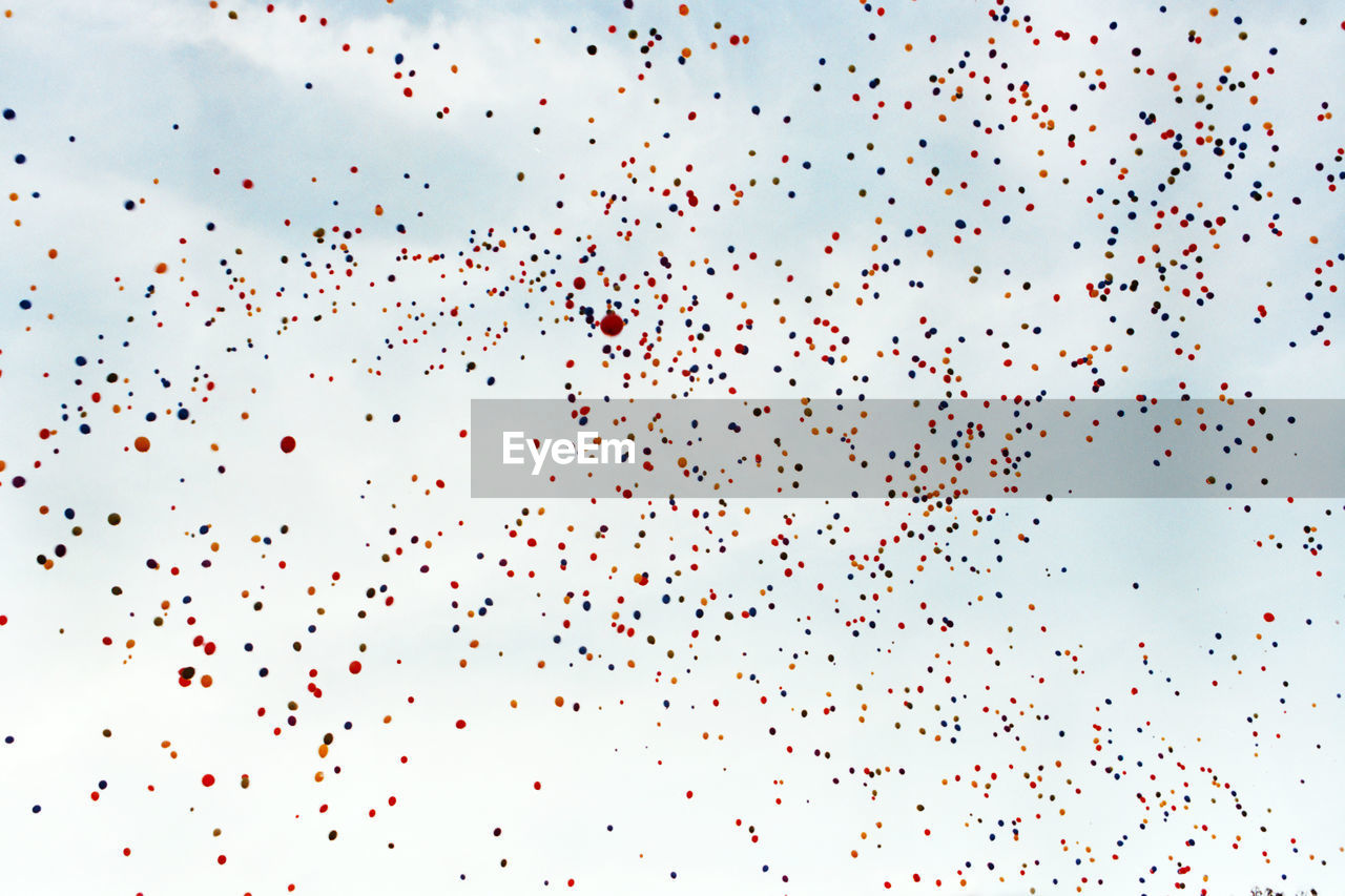 Low angle view of helium balloons flying against sky