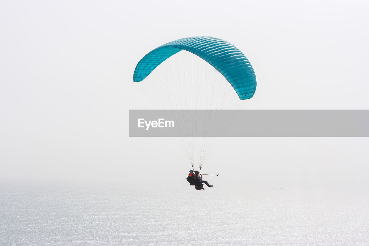 High angle view of people paragliding over ocean against clear sky