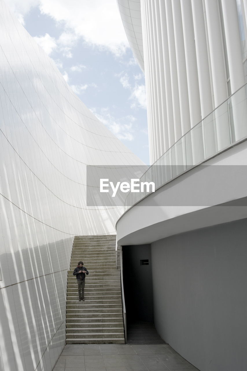 REAR VIEW OF MAN WALKING ON BUILDING AGAINST SKY