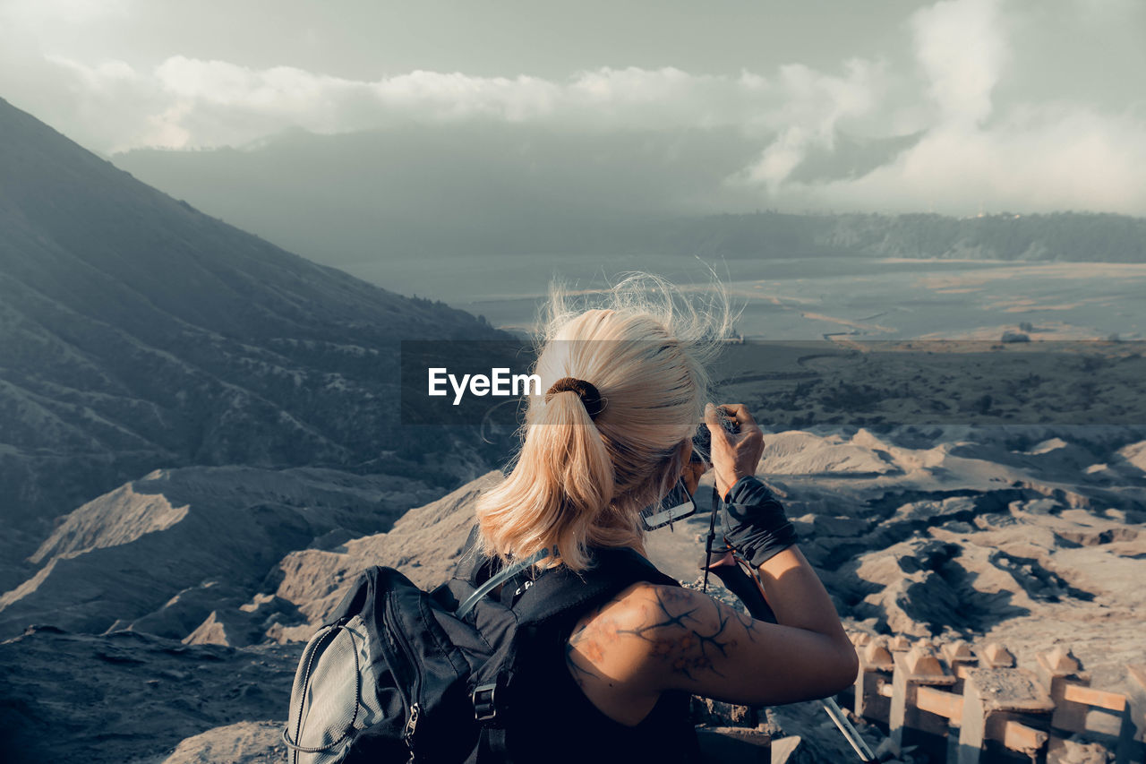 Side view of woman photographing on mountain against sky