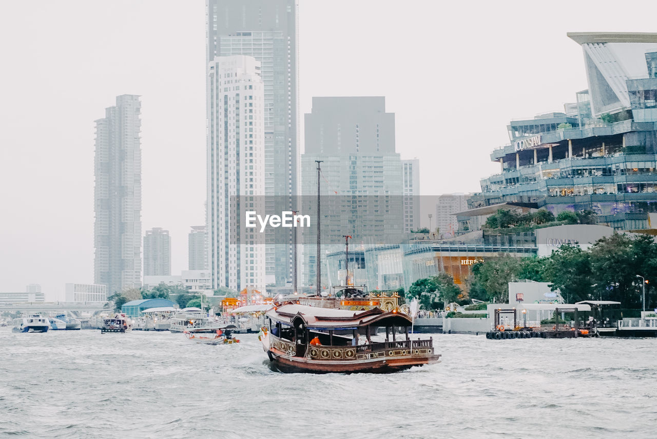 BOATS IN CITY BY BUILDINGS AGAINST SKY