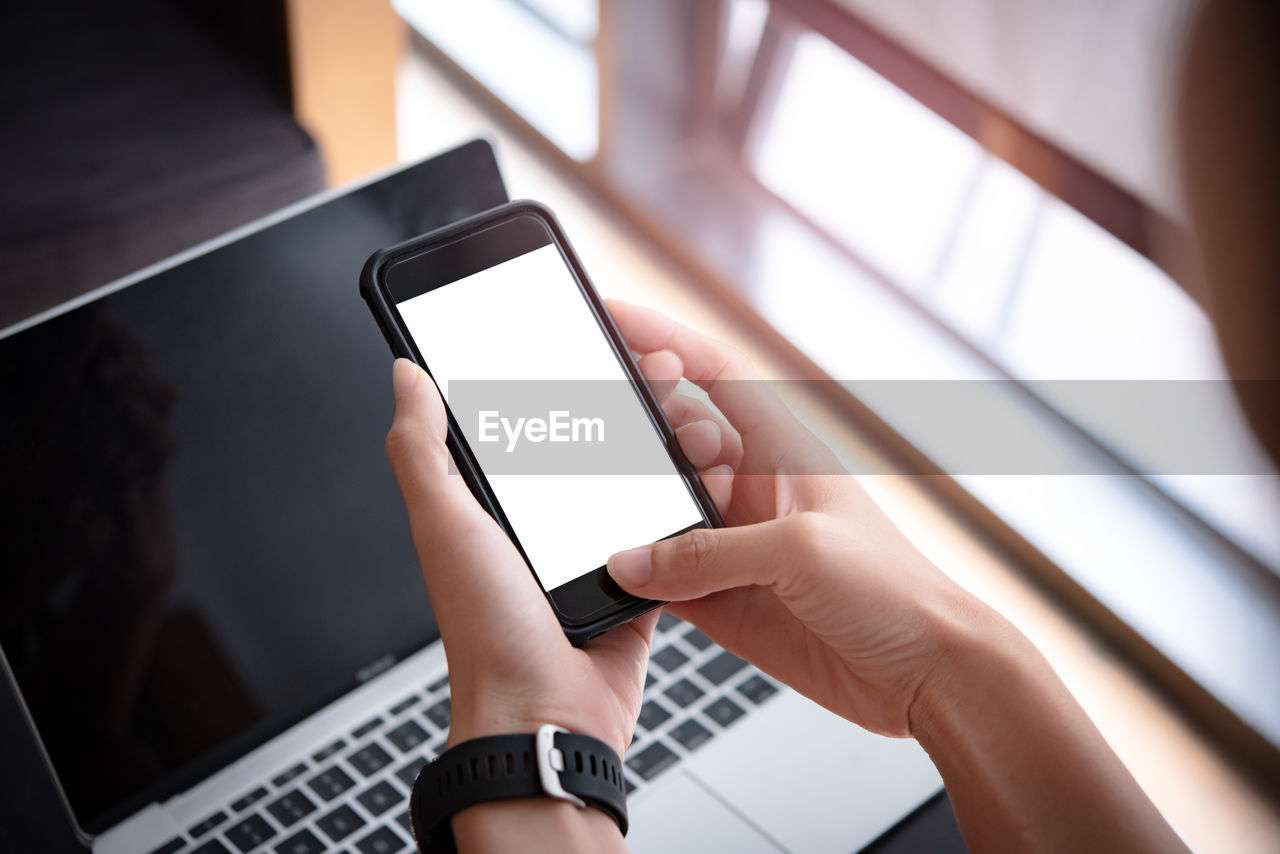Cropped hands of businesswoman using blank phone in office