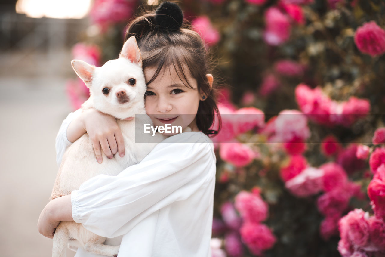 Happy child girl 3-4 year old holding pet dog over nature background closeup. looking at camera. 