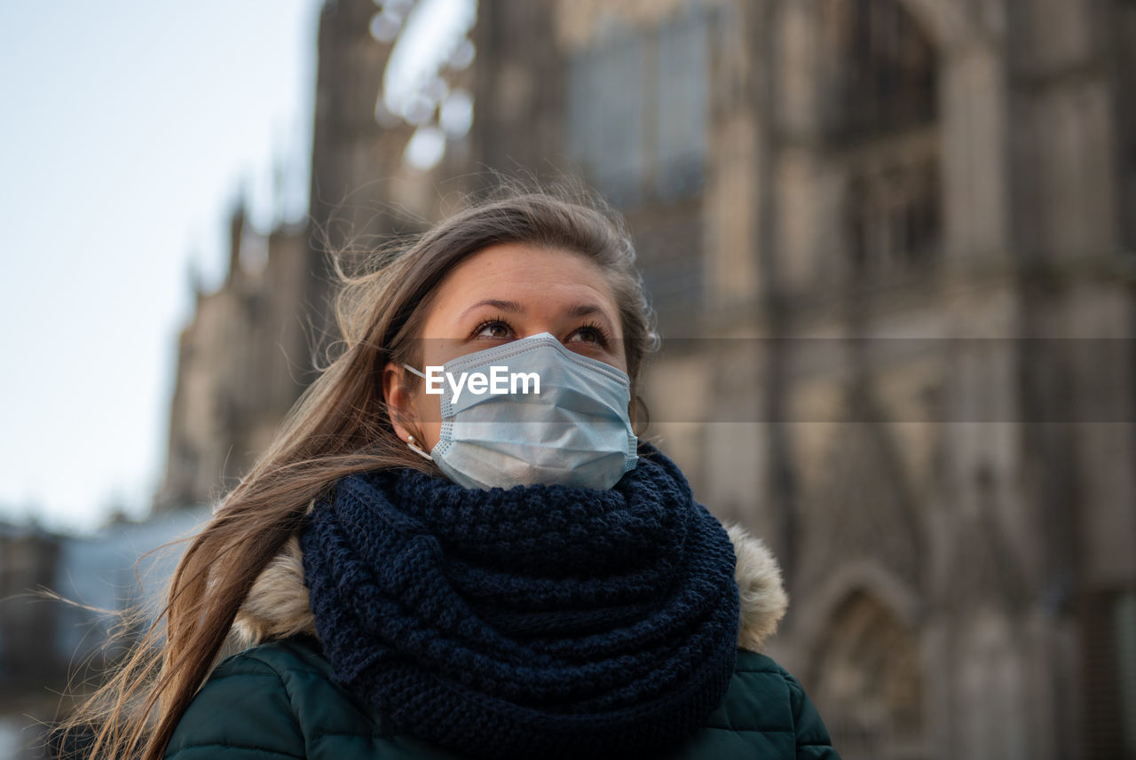Close-up of woman wearing flu mask looking away whiles standing outdoors