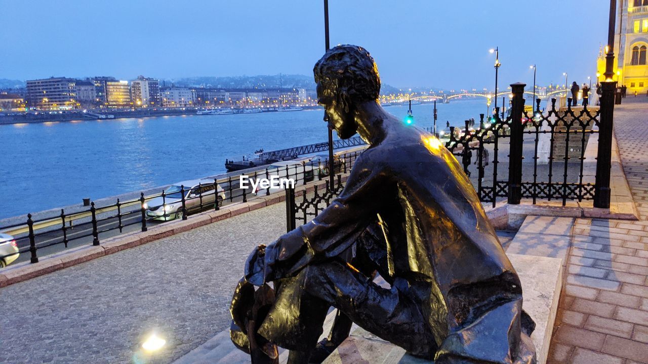 MAN SITTING ON RAILING BY RIVER IN CITY