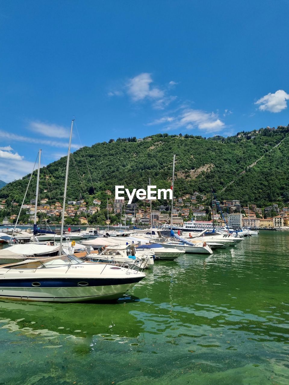 BOATS MOORED IN HARBOR AT SHORE AGAINST SKY