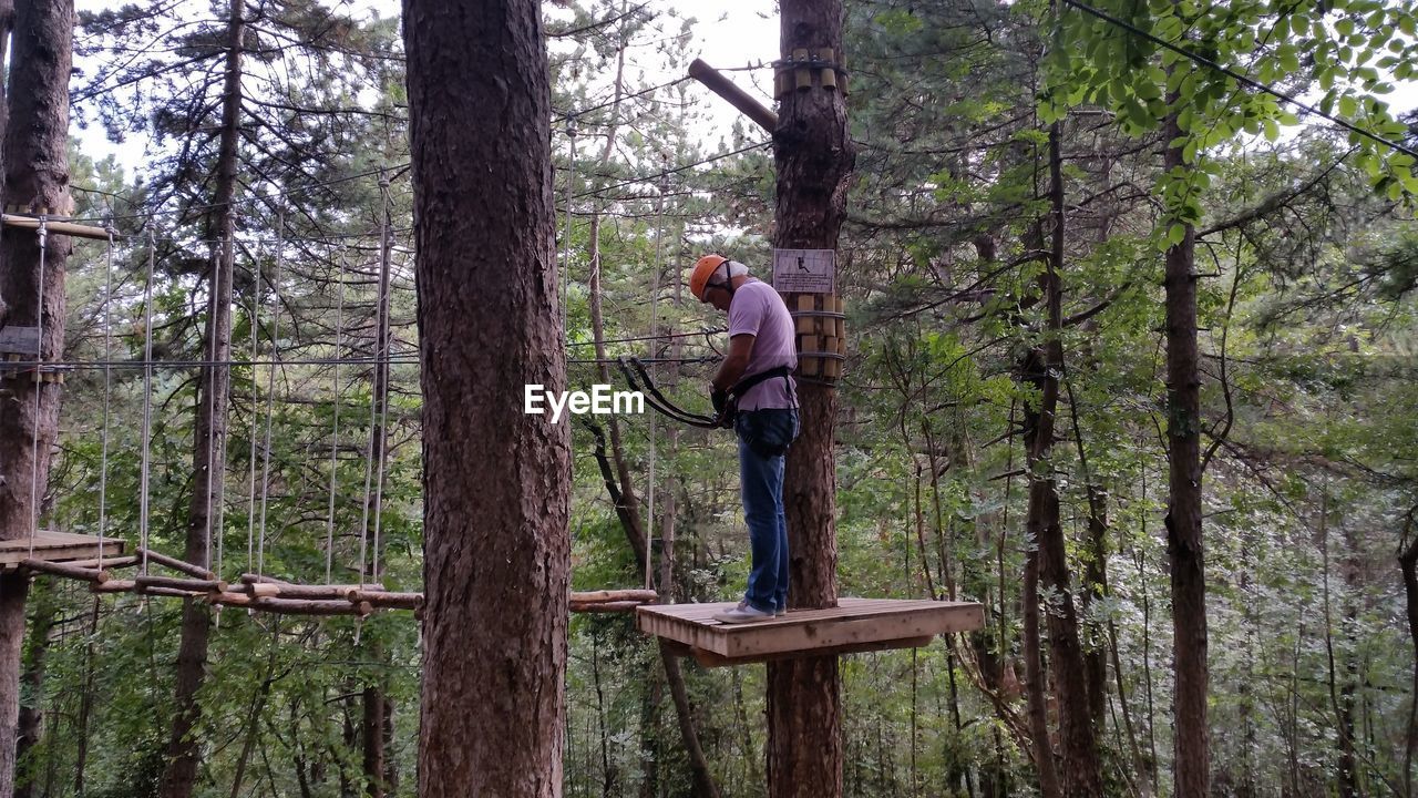 Man with zip line equipment standing on wooden platform at forest