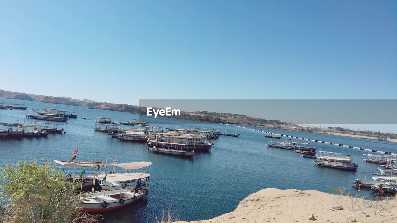 HIGH ANGLE VIEW OF BOATS MOORED ON SEA AGAINST CLEAR SKY