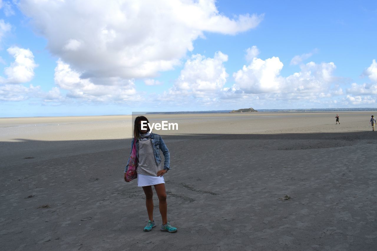 Woman standing at beach against cloudy sky