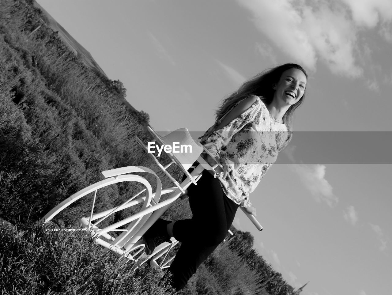 Low angle view of smiling woman standing by bicycle against sky