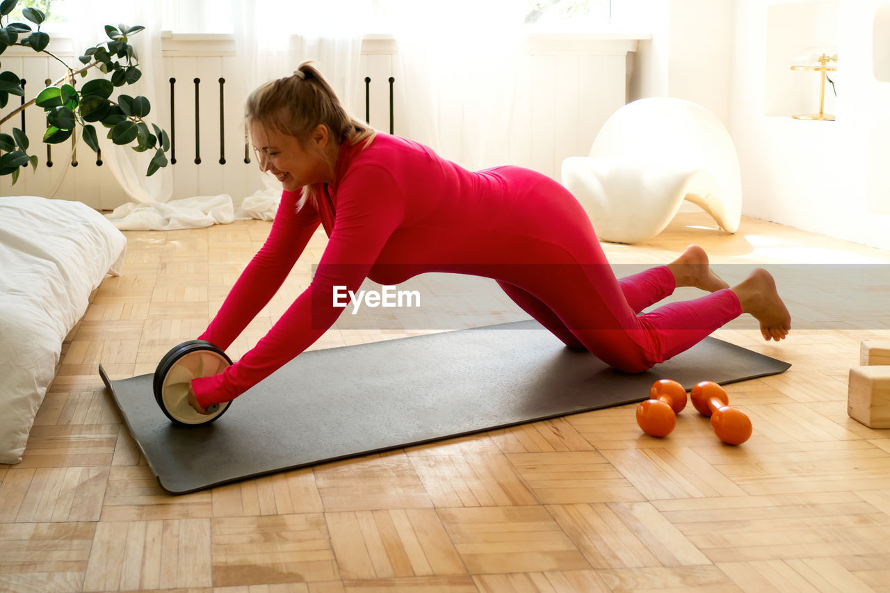 full length of young woman exercising on floor at home