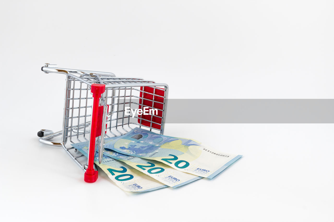 High angle view of paper currency with shopping cart over white background