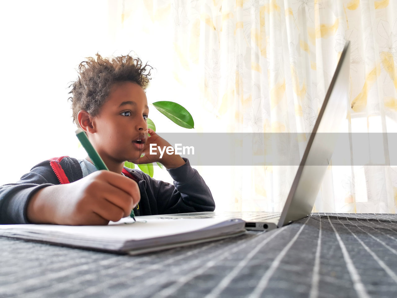 Cute boy with laptop studying on table a home