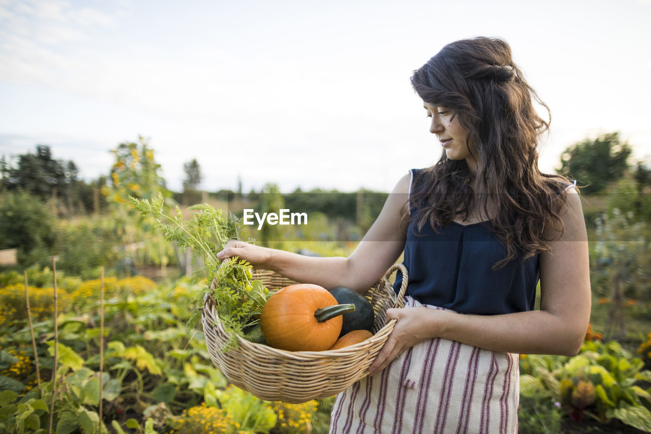 Woman looking at vegetables while carrying it in basket at community garden