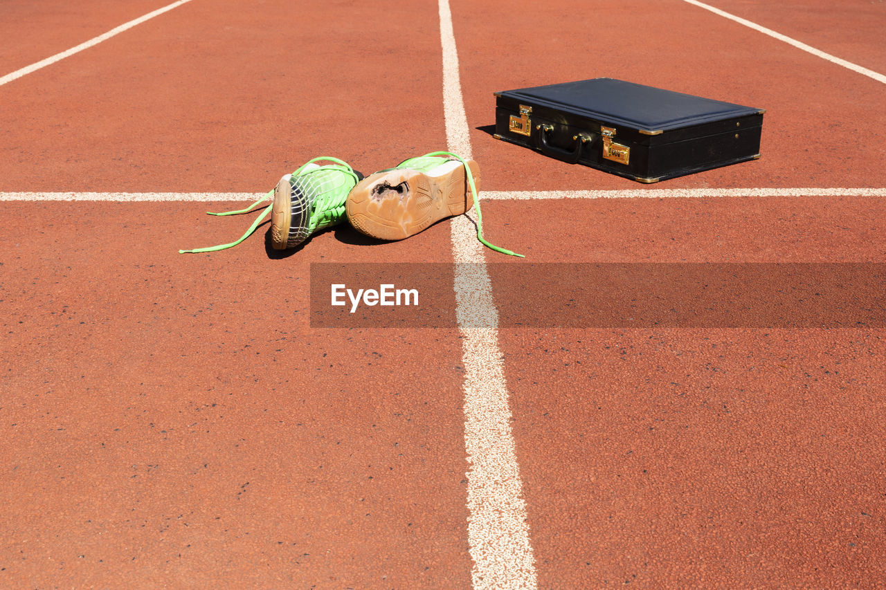A briefcase and broken running shoes on a running track symbolizing competition and in business