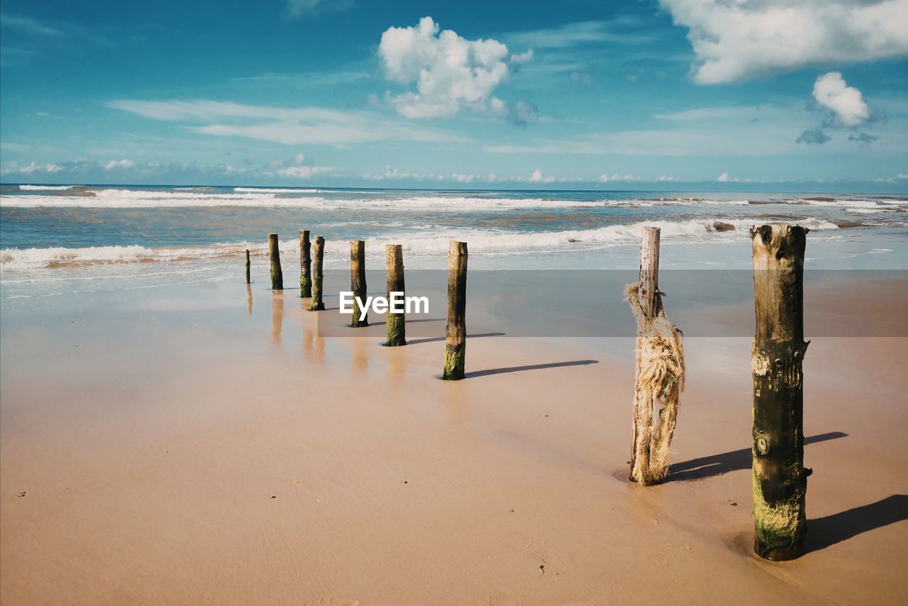 WOODEN POSTS ON SEA AGAINST SKY