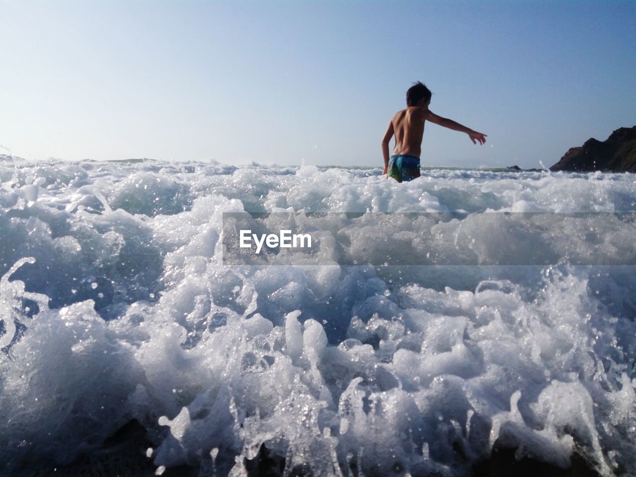 Rear view of shirtless boy standing in sea against sky during sunny day