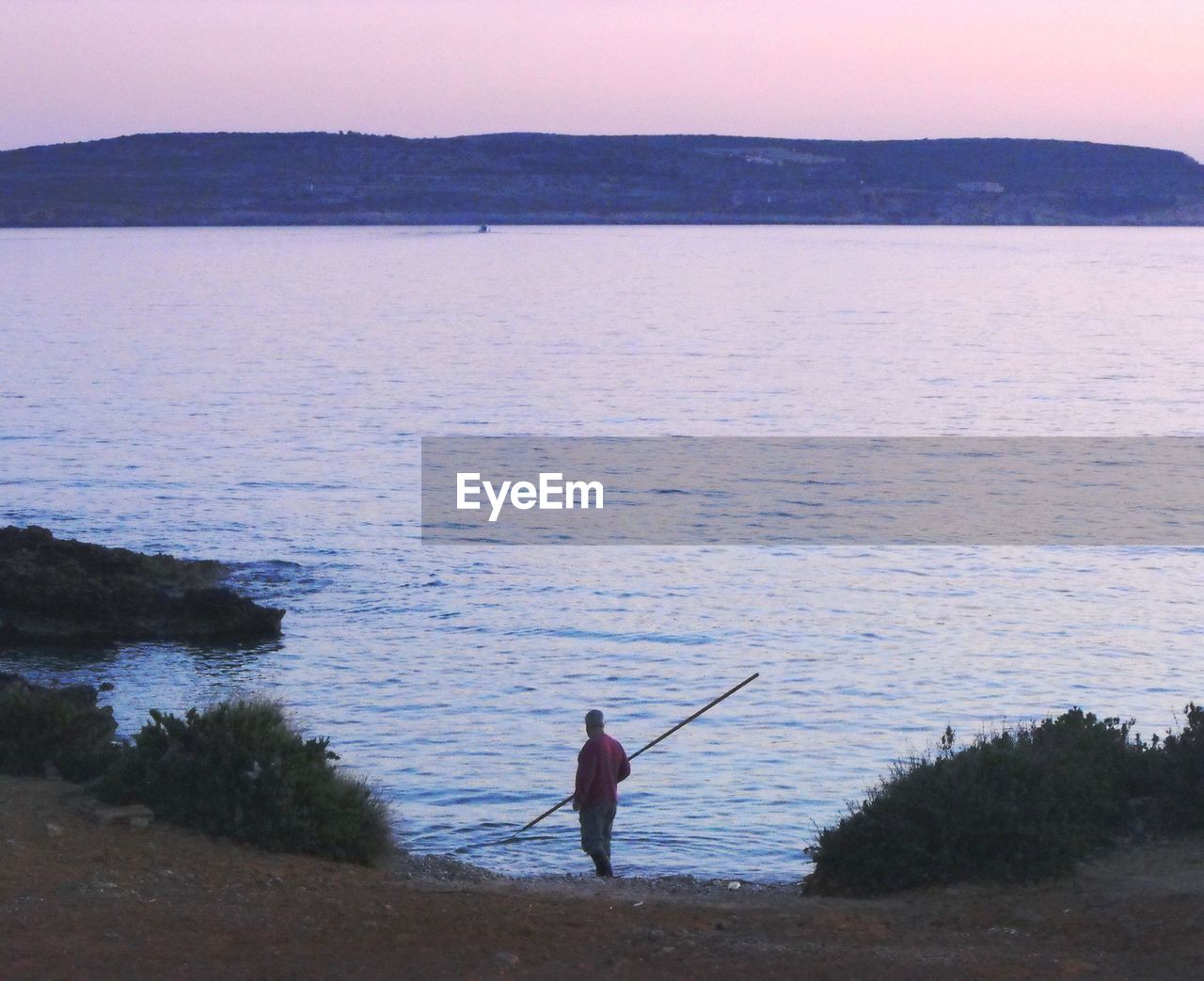 High angle view of man with stick standing at lakeshore