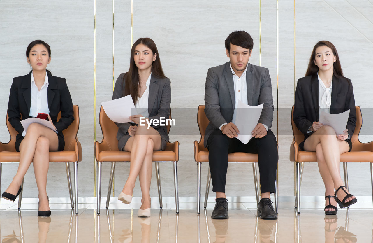 Full length of candidates holding papers while sitting on chairs in office