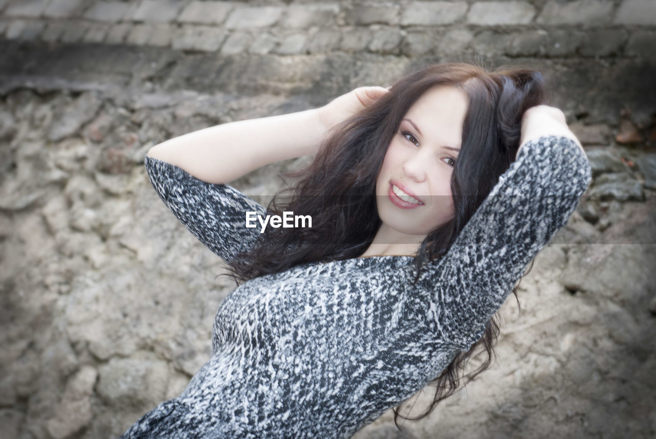 Portrait of smiling young woman with hands in hair against wall