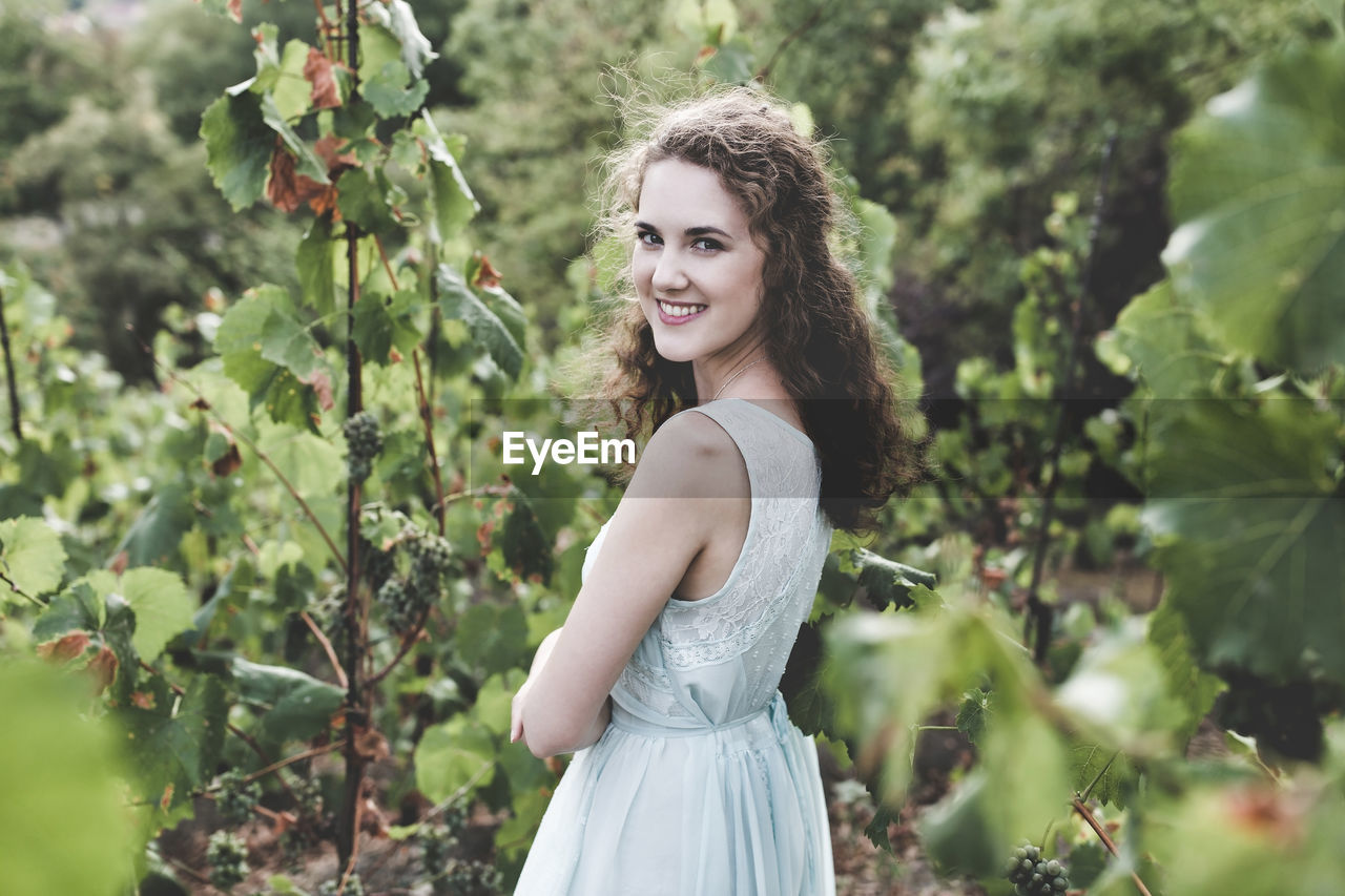 Beautiful smiling curly hair brunette in a light blue simple dress in a vineyard