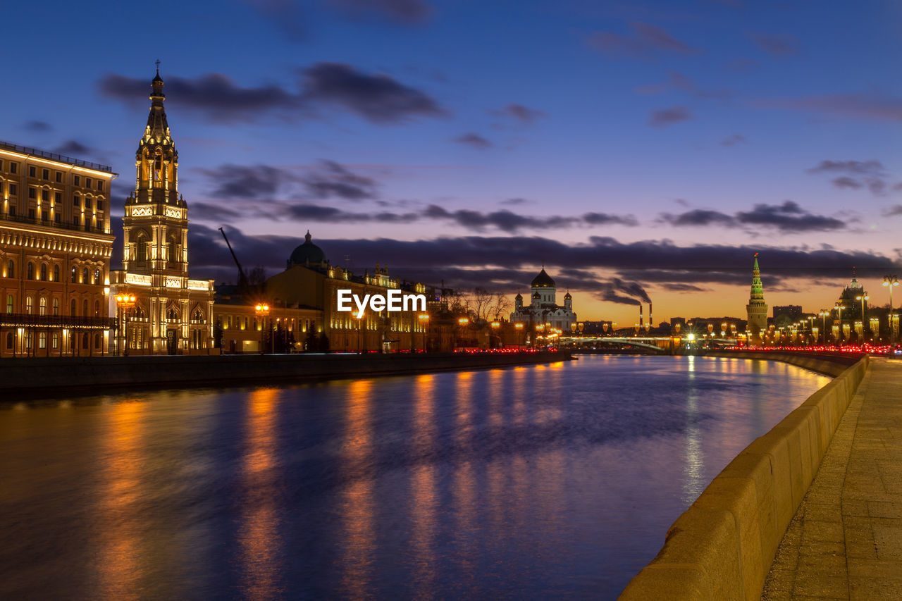 ILLUMINATED BUILDINGS BY RIVER AGAINST SKY