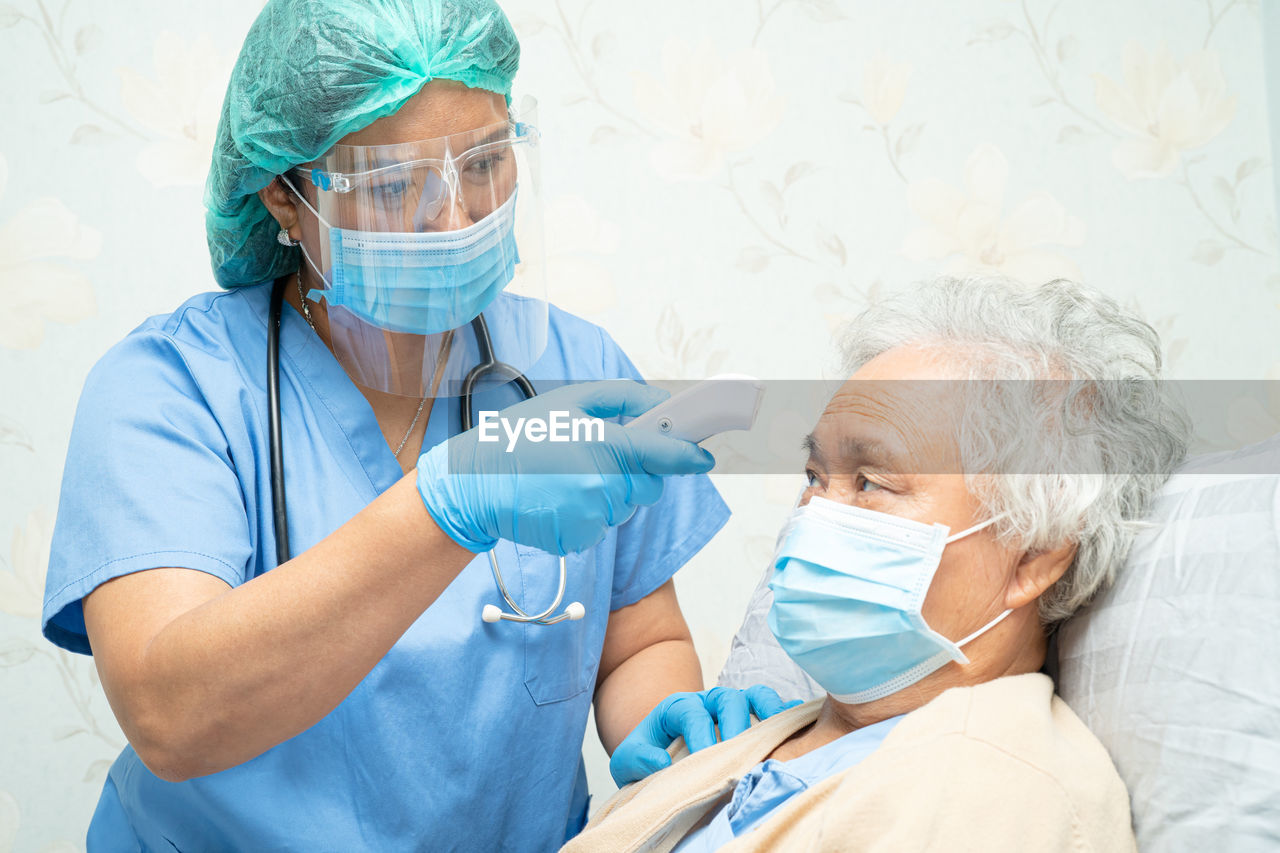 Doctor wearing mask checking temperature of patient at hospital