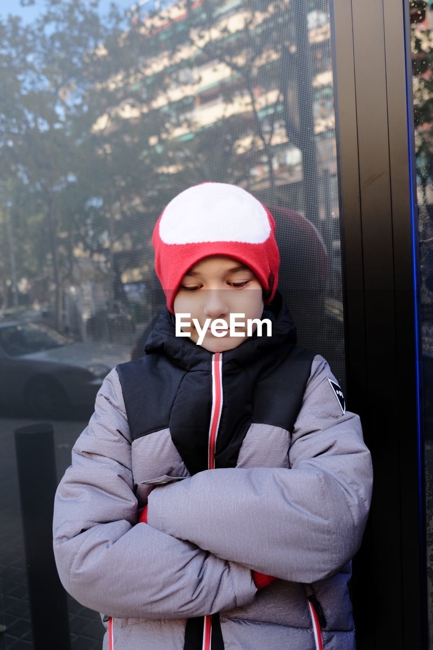 Close-up of boy in warm clothing standing against glass