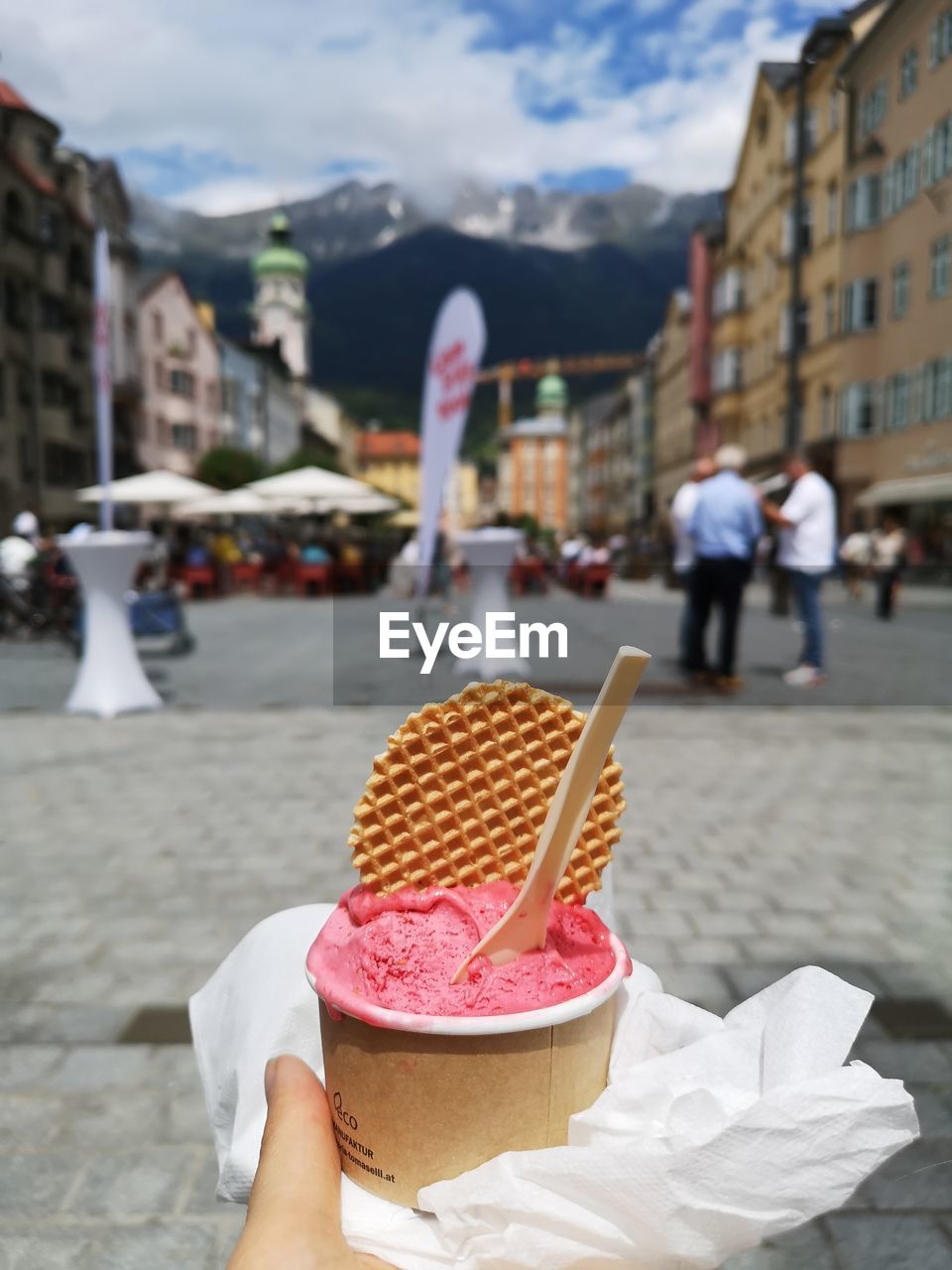 HAND HOLDING ICE CREAM CONE AGAINST BUILDINGS