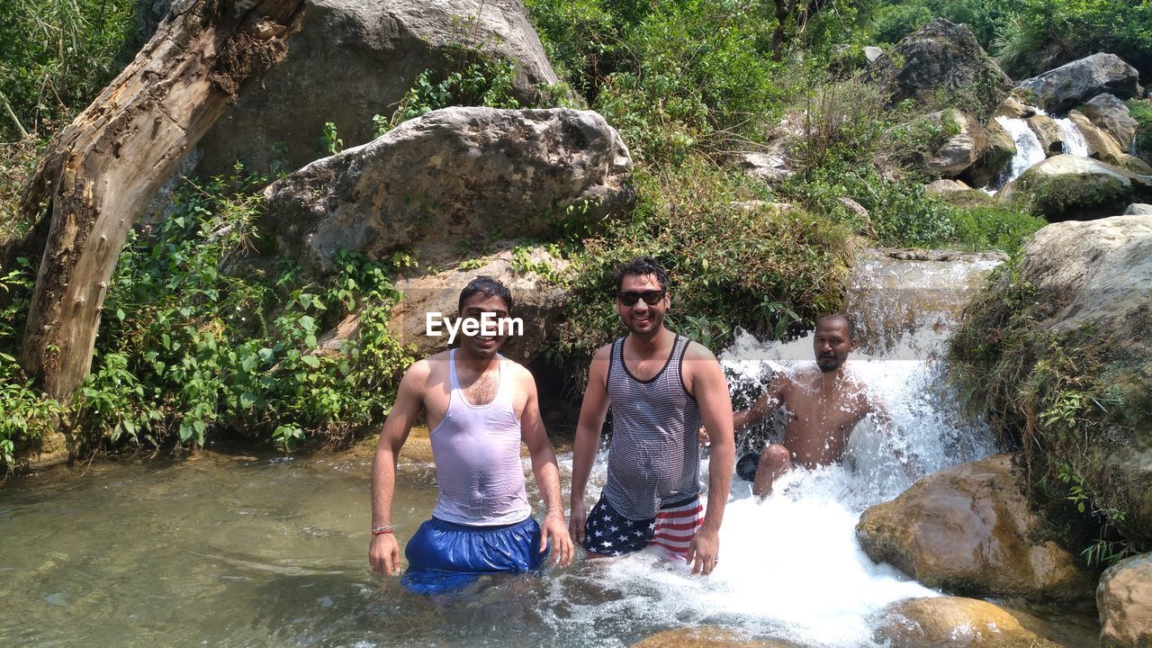 FULL LENGTH OF SHIRTLESS YOUNG WOMAN ON ROCK BY RIVER