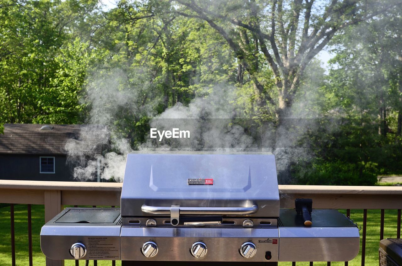 Electric barbecue grill steaming by railing against trees