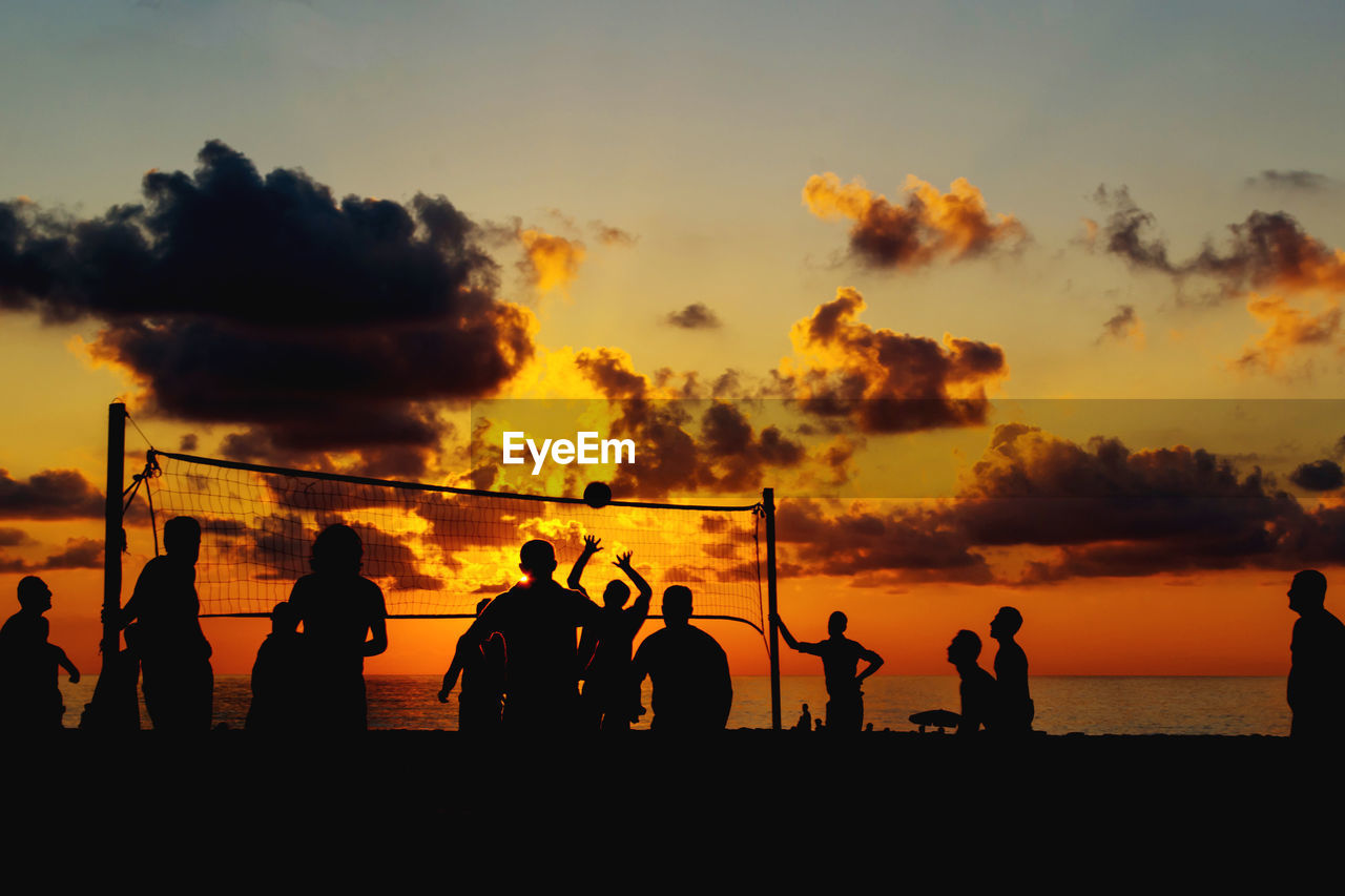 Silhouette people playing volleyball at beach against sky during sunset