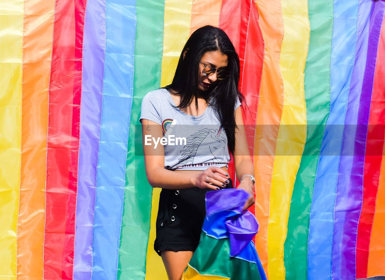 Young woman standing against rainbow flag