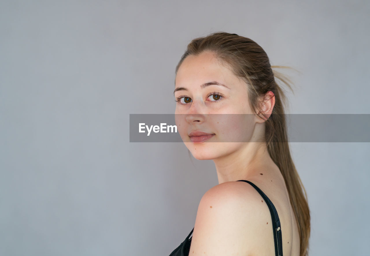 PORTRAIT OF A YOUNG WOMAN AGAINST GRAY BACKGROUND