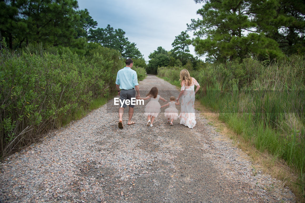 Rear view of family walking on dirt road amidst forest