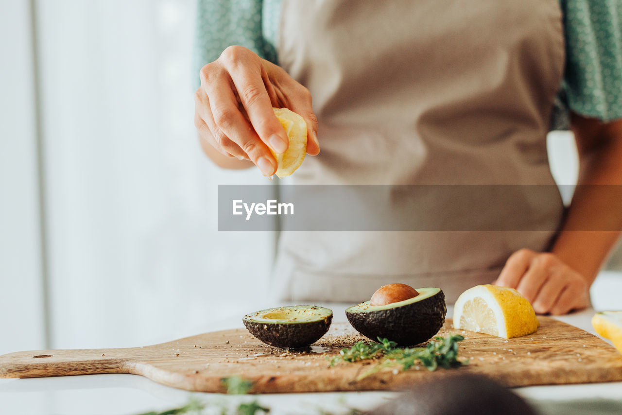 Female hands squeezing lemon on avocado while preparing healthy meal