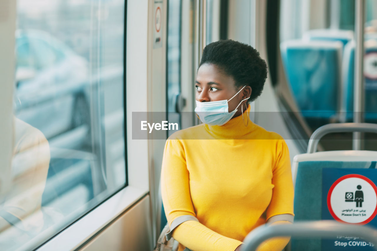 Dubai, uae, november 2020 a young african woman wearing a protective mask rides on a bus and looks