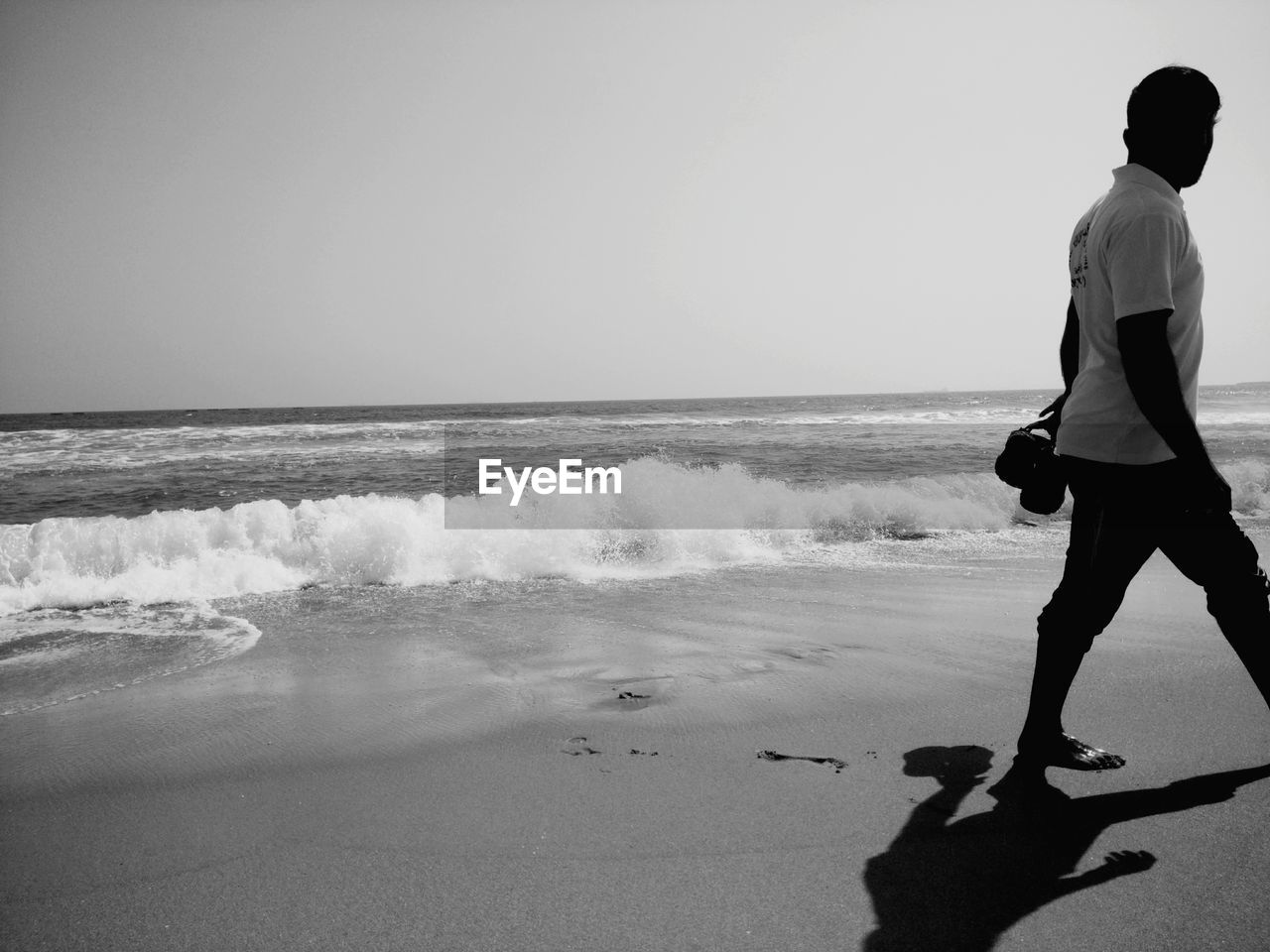 REAR VIEW OF PEOPLE STANDING ON BEACH AGAINST CLEAR SKY