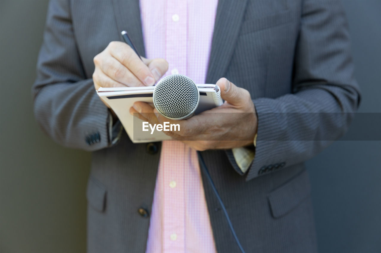 Journalist at news conference or media event, writing notes, holding microphone