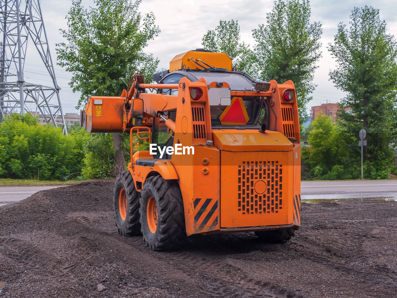 Orange color skid steer loader with a many purpose bucket is using in landscaping.