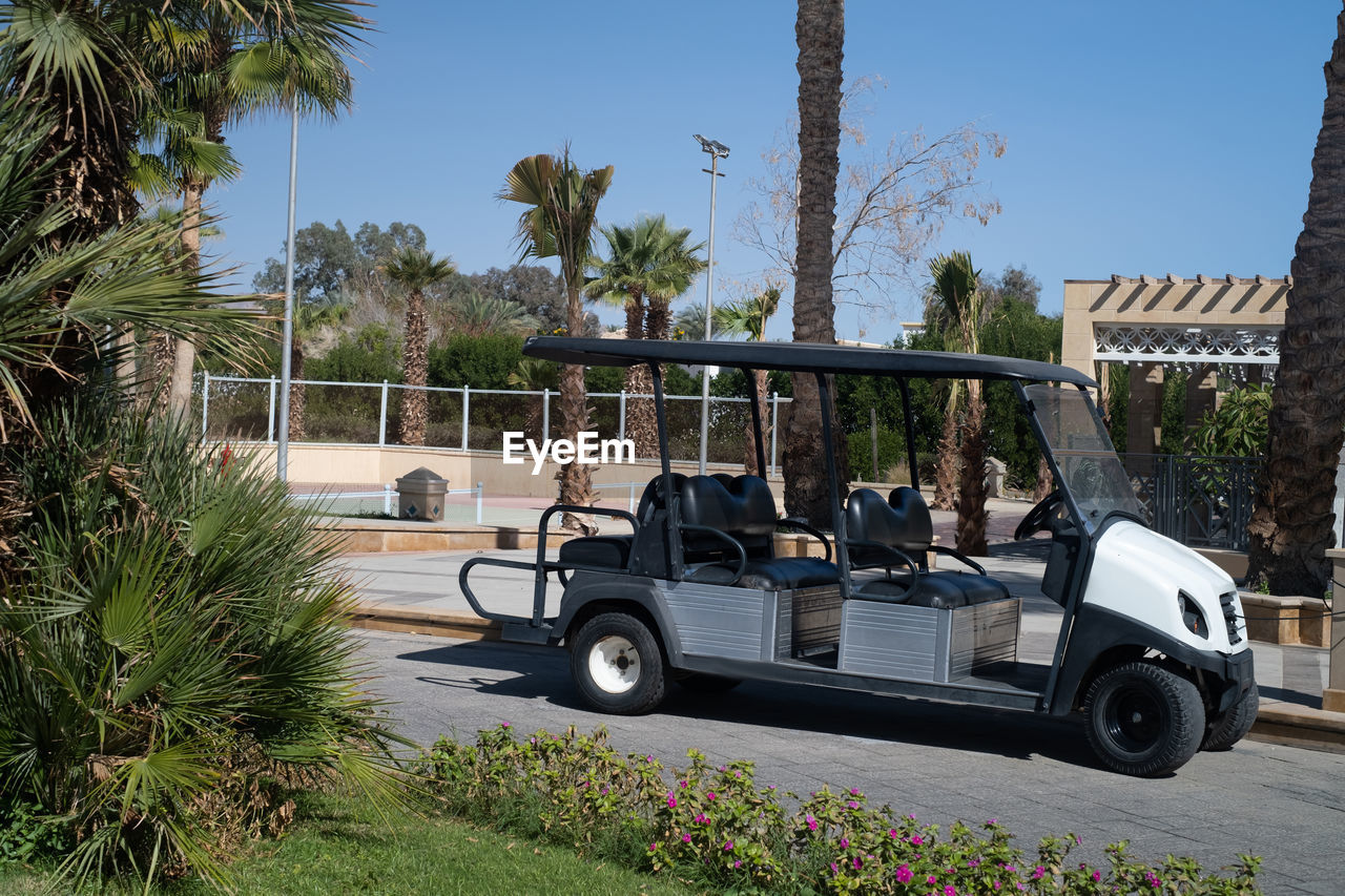 golf cart, plant, transportation, tree, golf, mode of transportation, palm tree, tropical climate, car, nature, vehicle, vacation, day, land vehicle, motor vehicle, leisure activity, grass, architecture, outdoors, sports, sky, golf course