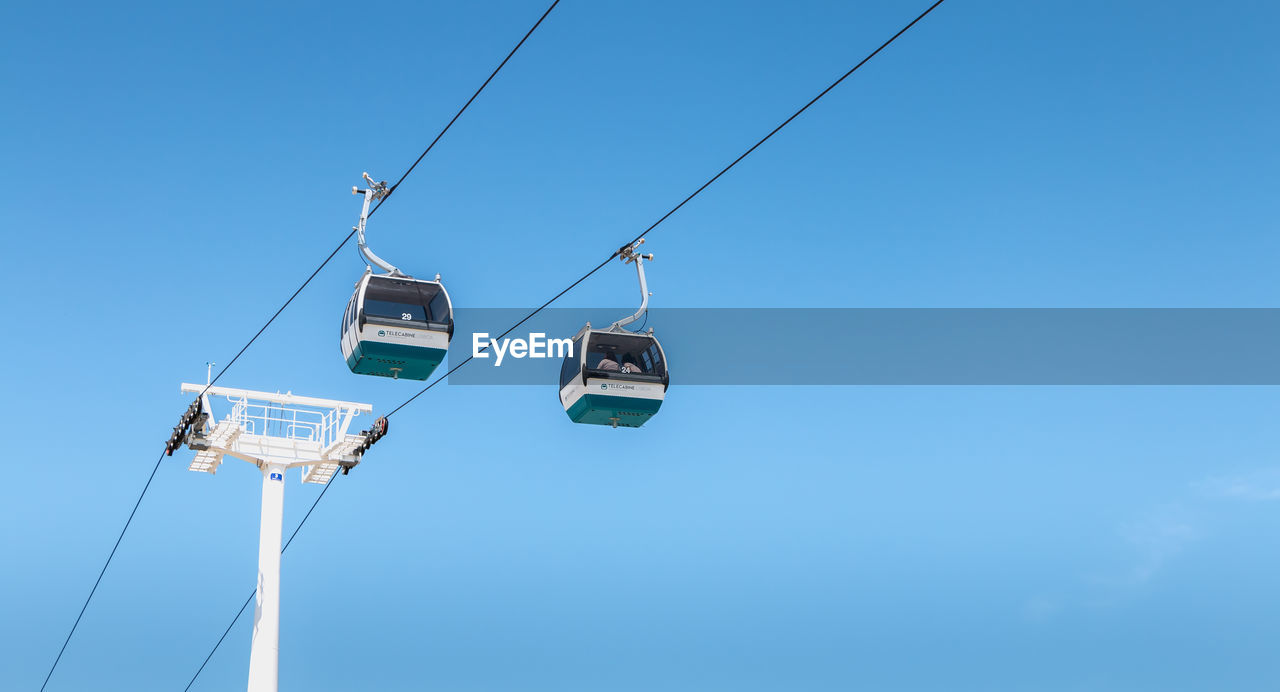 LOW ANGLE VIEW OF OVERHEAD CABLE CARS AGAINST CLEAR BLUE SKY