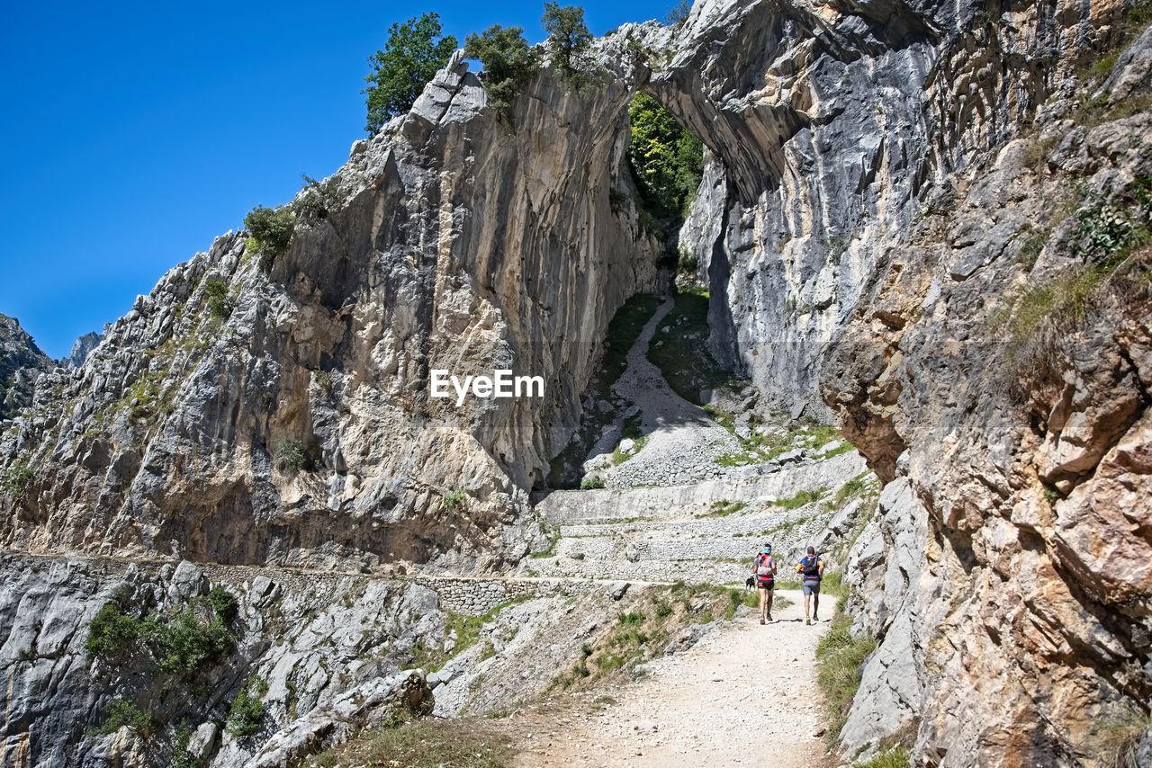 MAN STANDING ON CLIFF BY MOUNTAINS