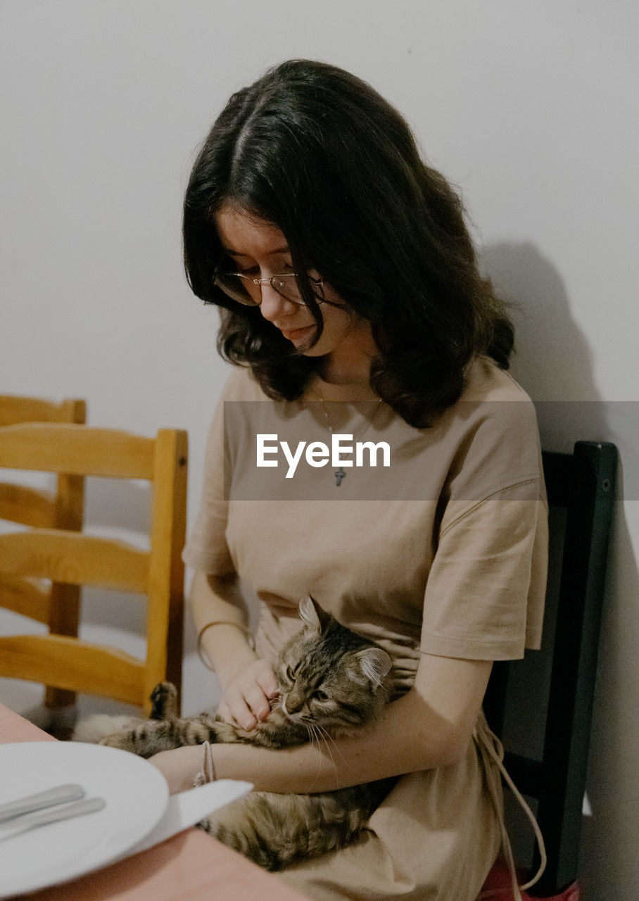 A teenage girl with a cat in her arms sits at the table.