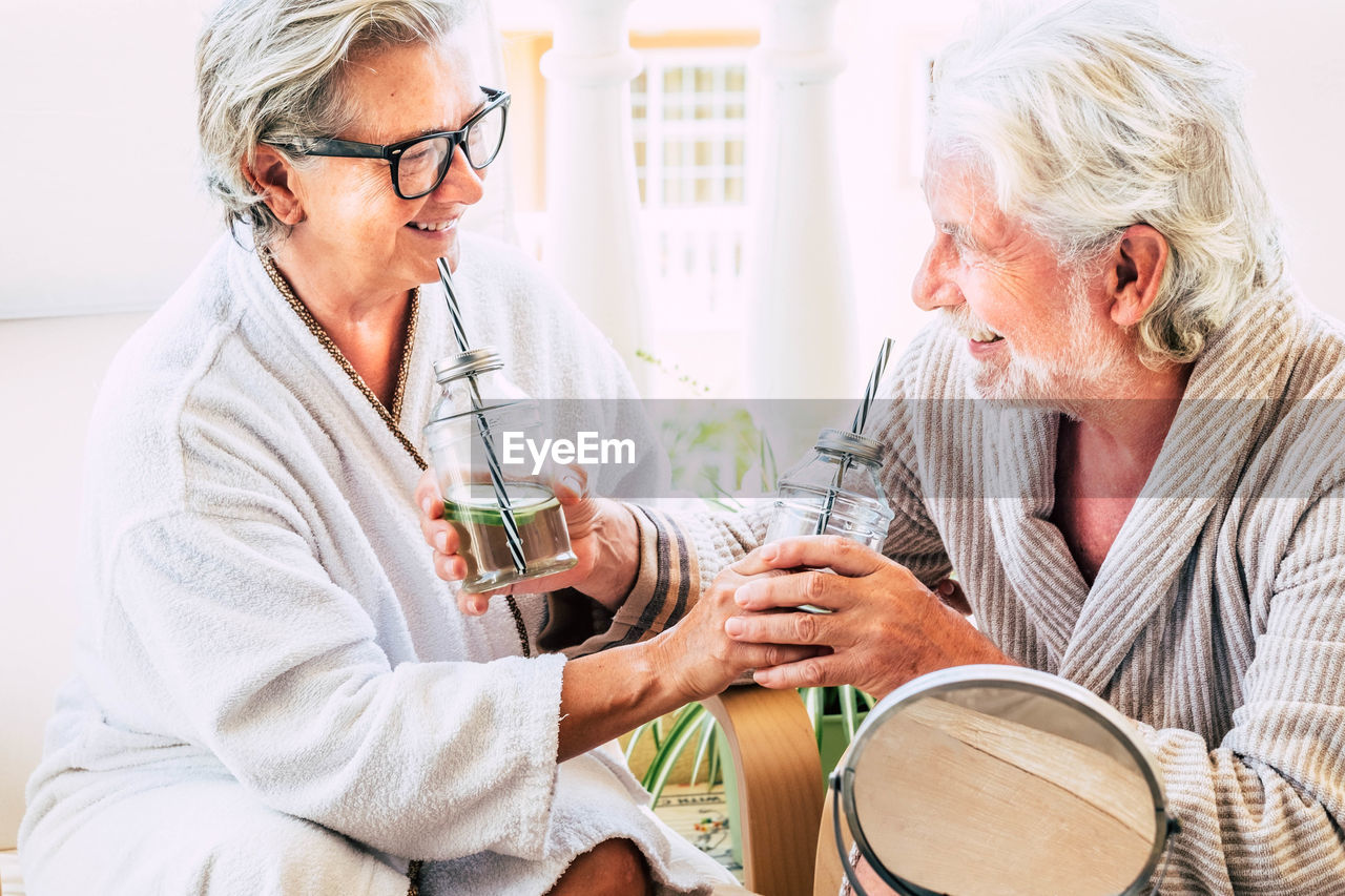 Senior couple in bathrobes enjoying drinks at hotel