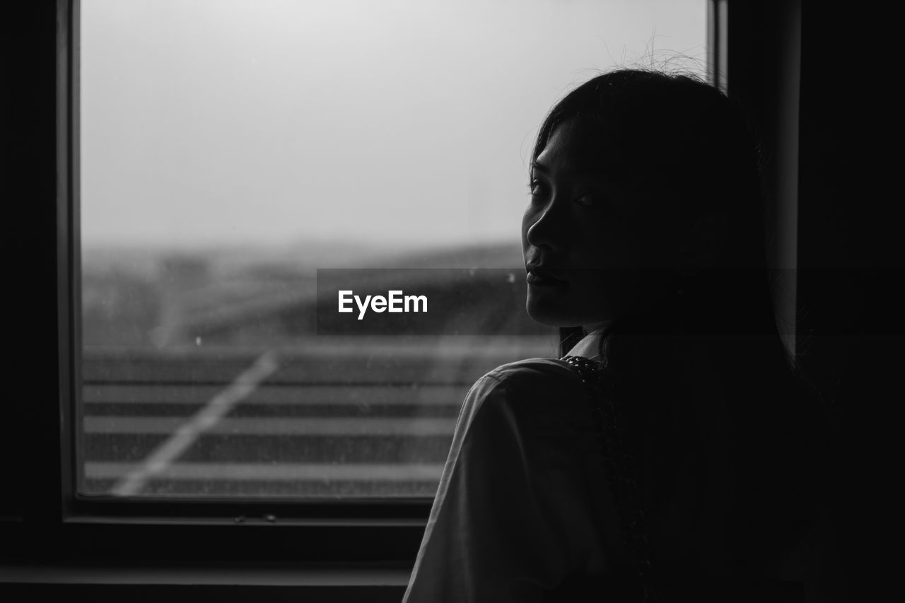 Portrait of woman looking over shoulder while standing against window at home